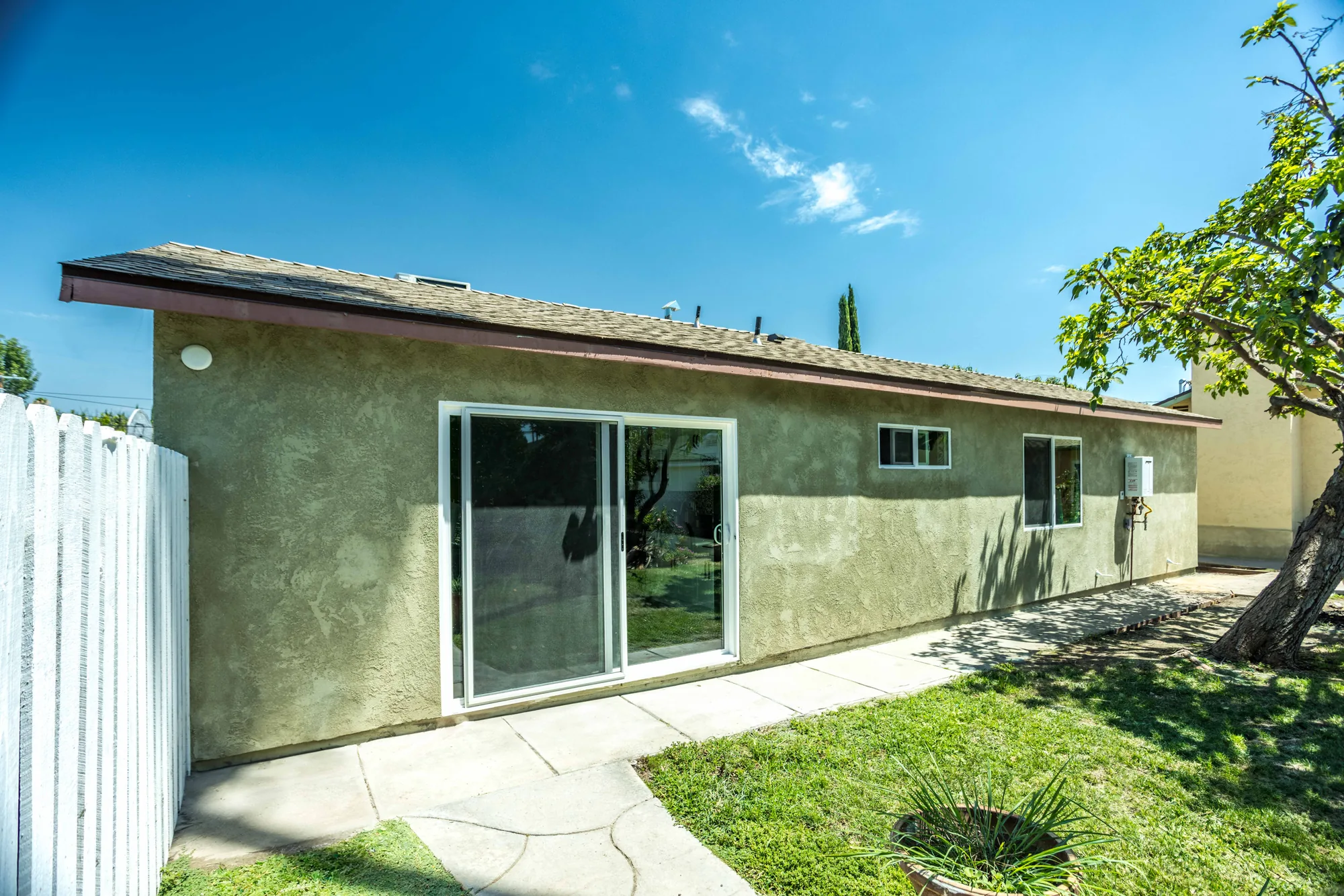 Side elevation of the stucco addition with a sliding glass door, windows, and a concrete patio.