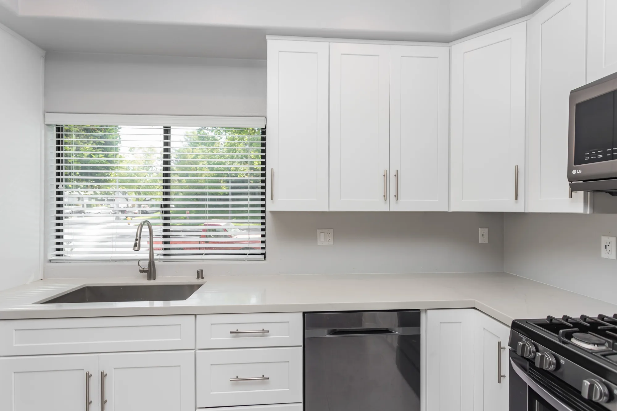 Kitchen sink run below a blinded window with white upper cabinets and a stainless dishwasher alongside.