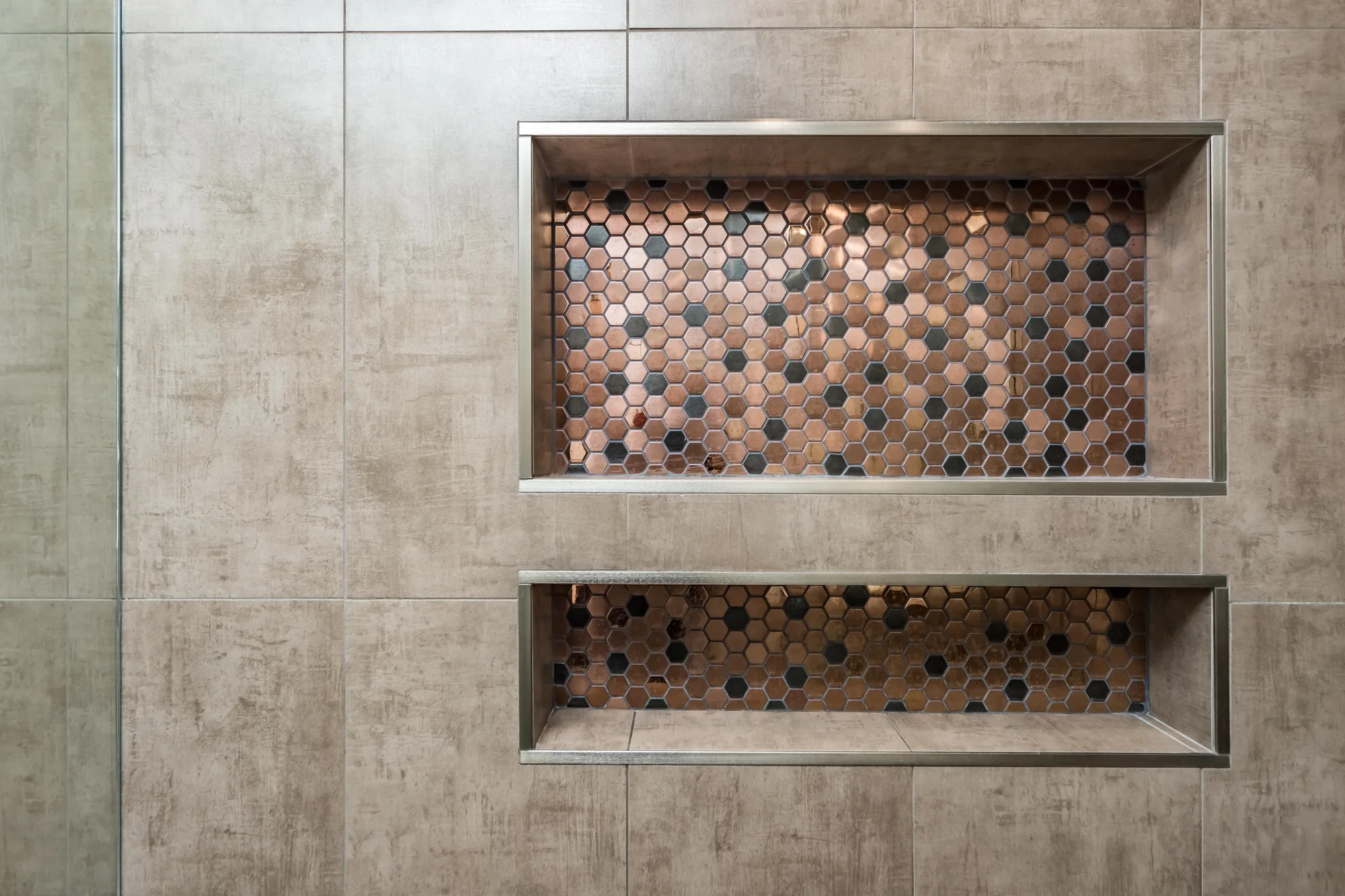 Two stacked shower niches with metal edge trim and copper-tone hexagon mosaic backing.