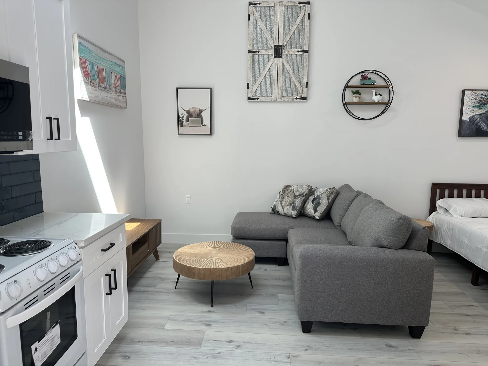 View from the kitchenette across a studio unit's seating area toward the bed and plank flooring.