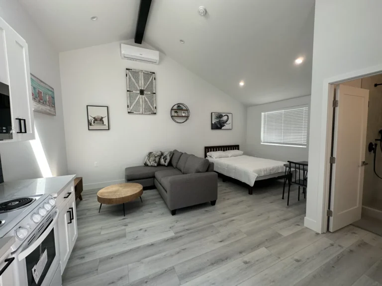 Open studio ADU with vaulted ceiling, gray sectional sofa, bed and gray wood-look plank flooring.