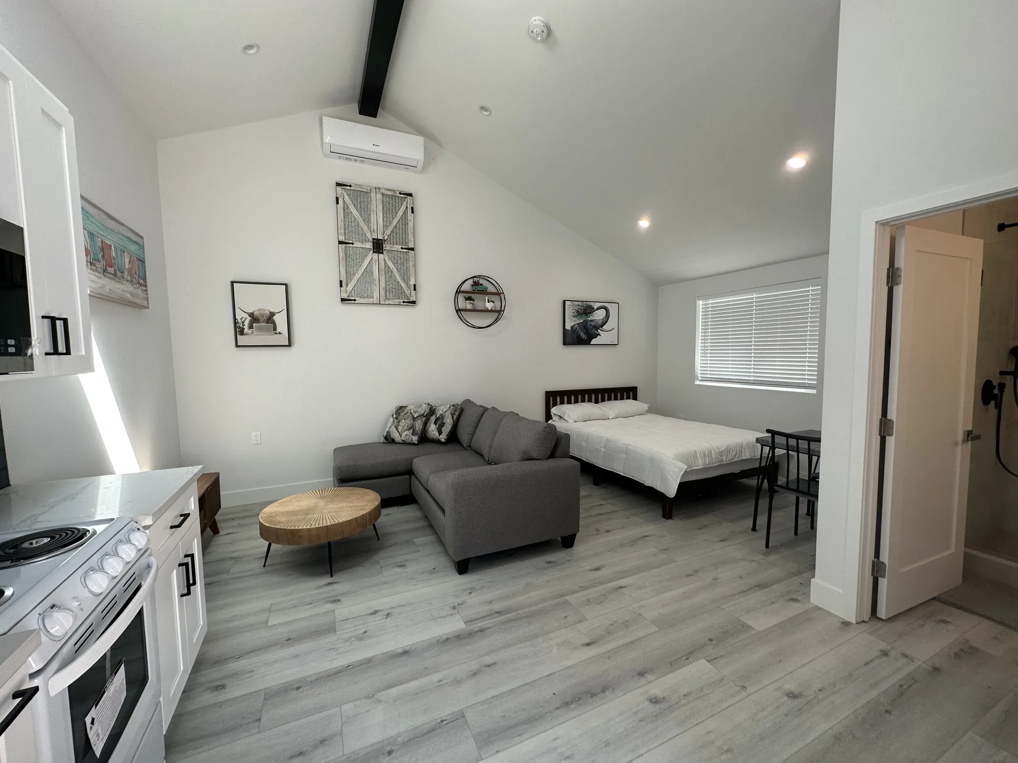 Open studio ADU with vaulted ceiling, gray sectional sofa, bed and gray wood-look plank flooring.