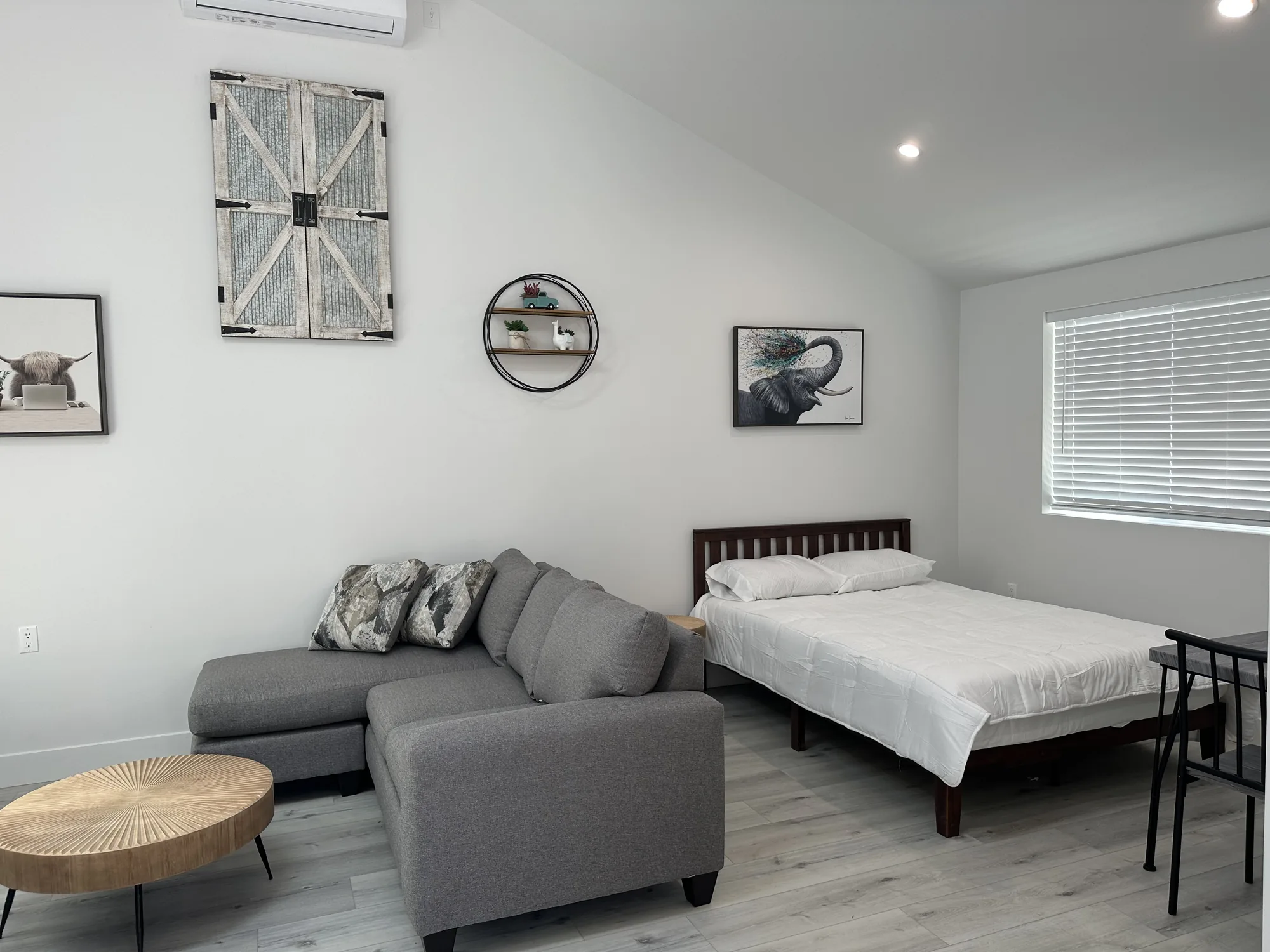 Wide view of a studio ADU showing sectional seating, a bed and a wall-mounted mini-split unit.