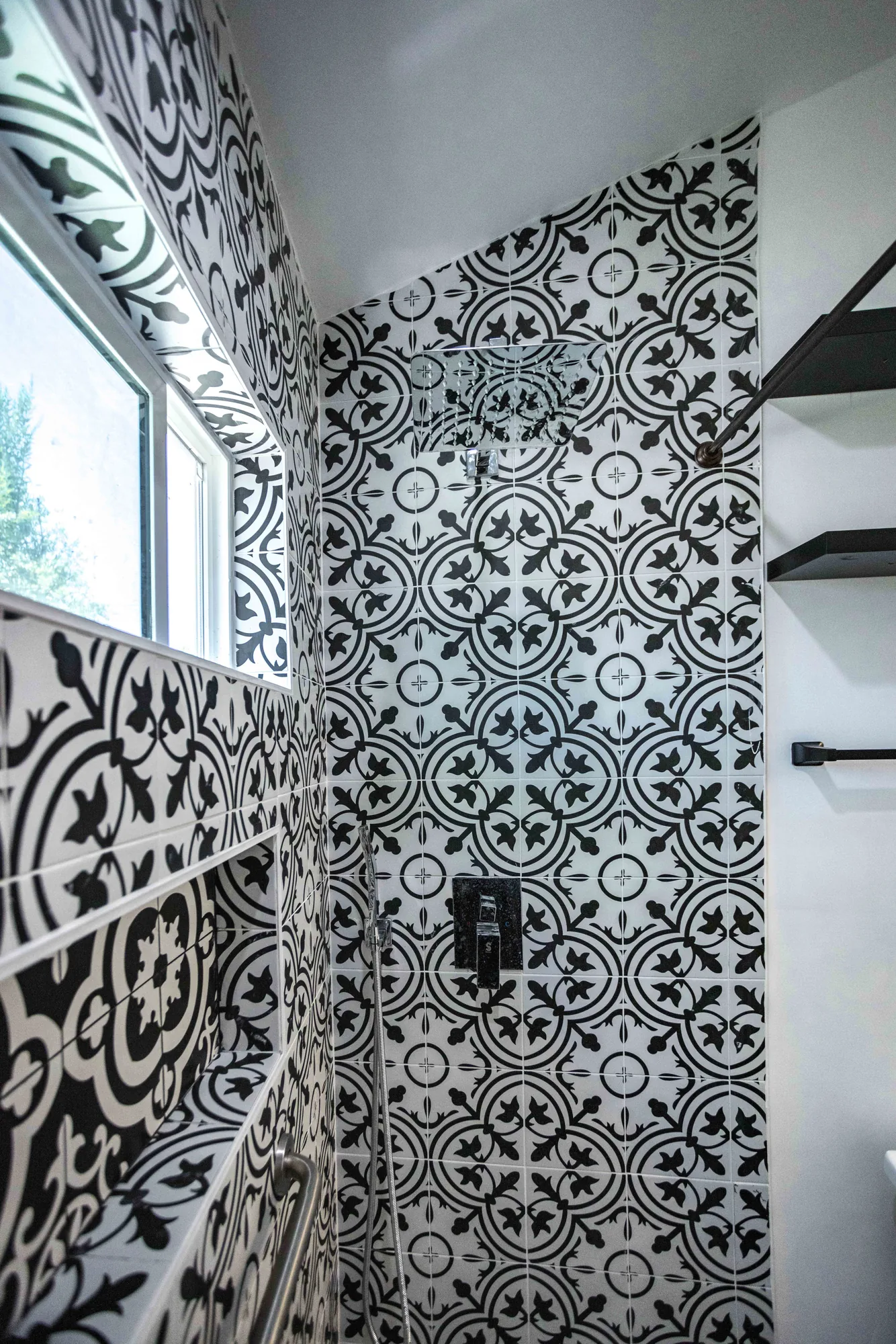 Tiled shower stall with a small window, black valve trim, and floating shelves on the adjacent wall.