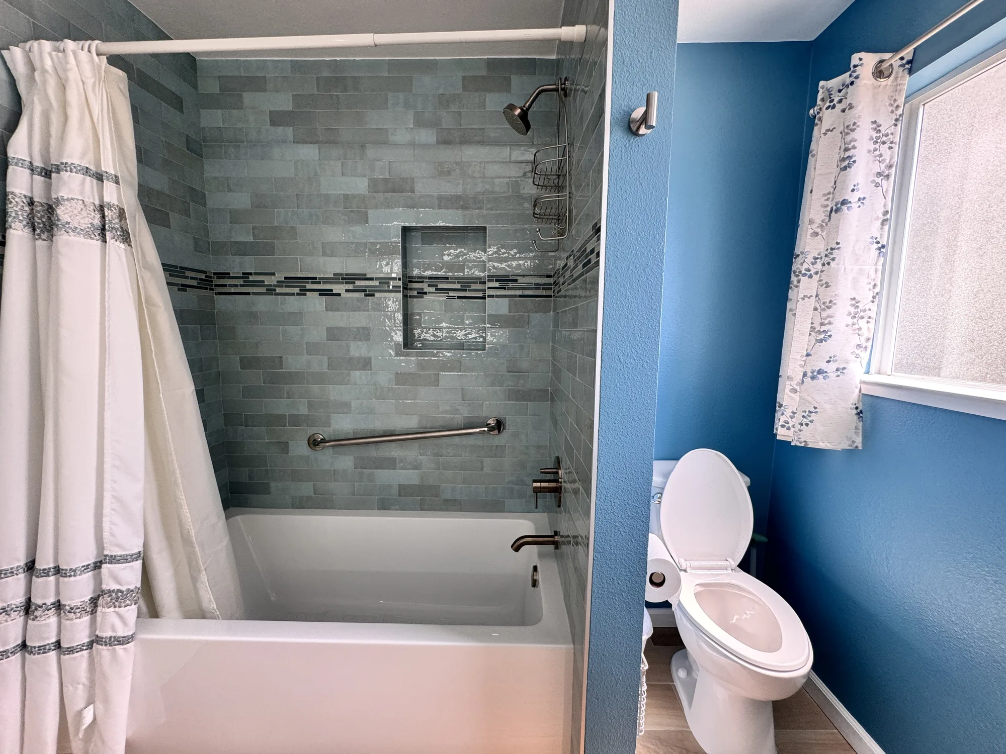 Wide view showing the tiled tub and shower on the left and the blue toilet alcove on the right.
