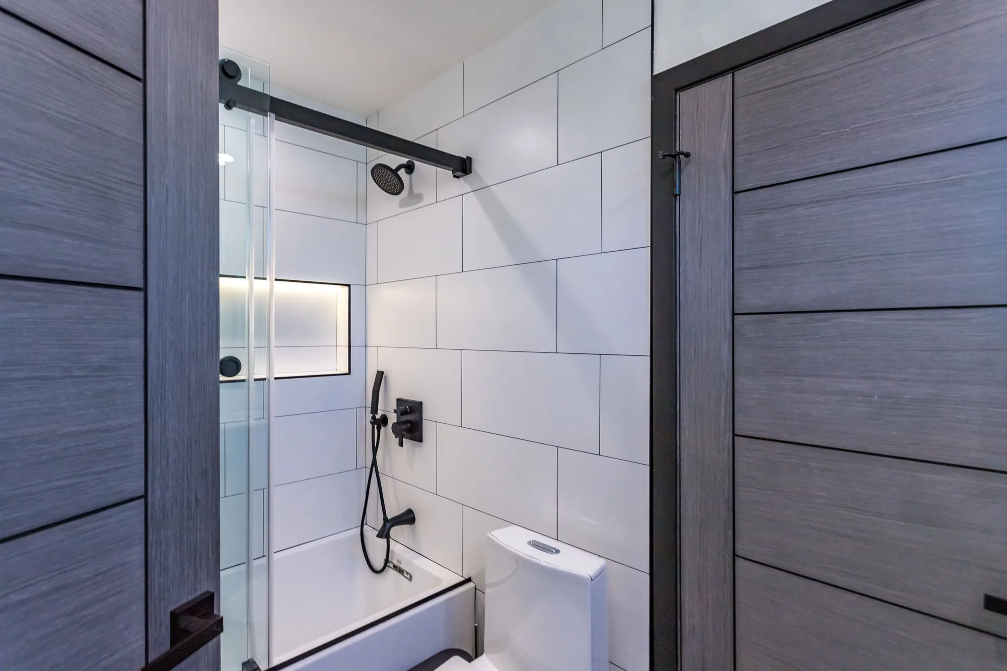 Tub and shower alcove with white large-format tile, sliding glass door and matte black fixtures.
