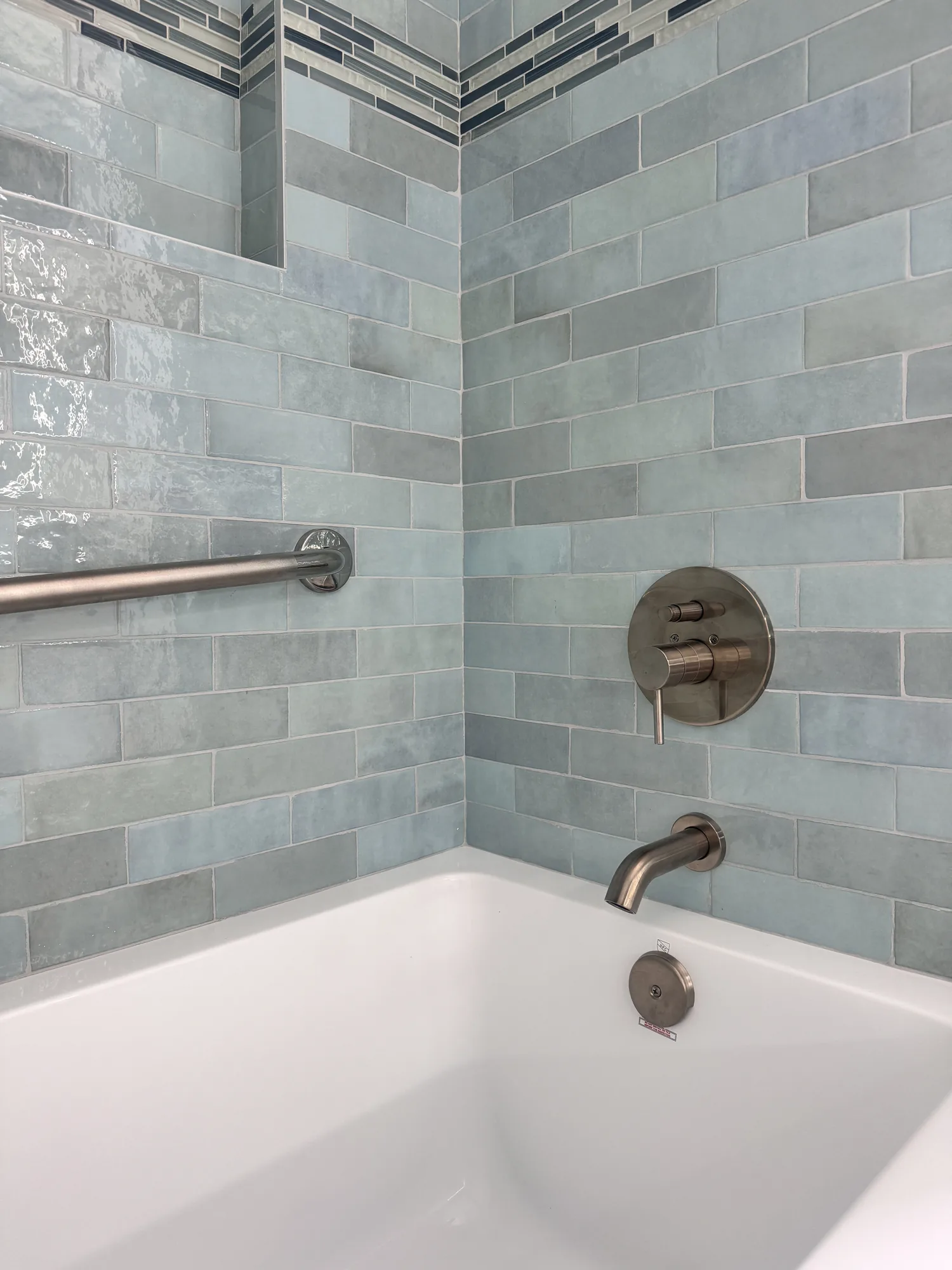 Close detail of the brushed nickel tub spout, valve trim and grab bar against blue-green tile.
