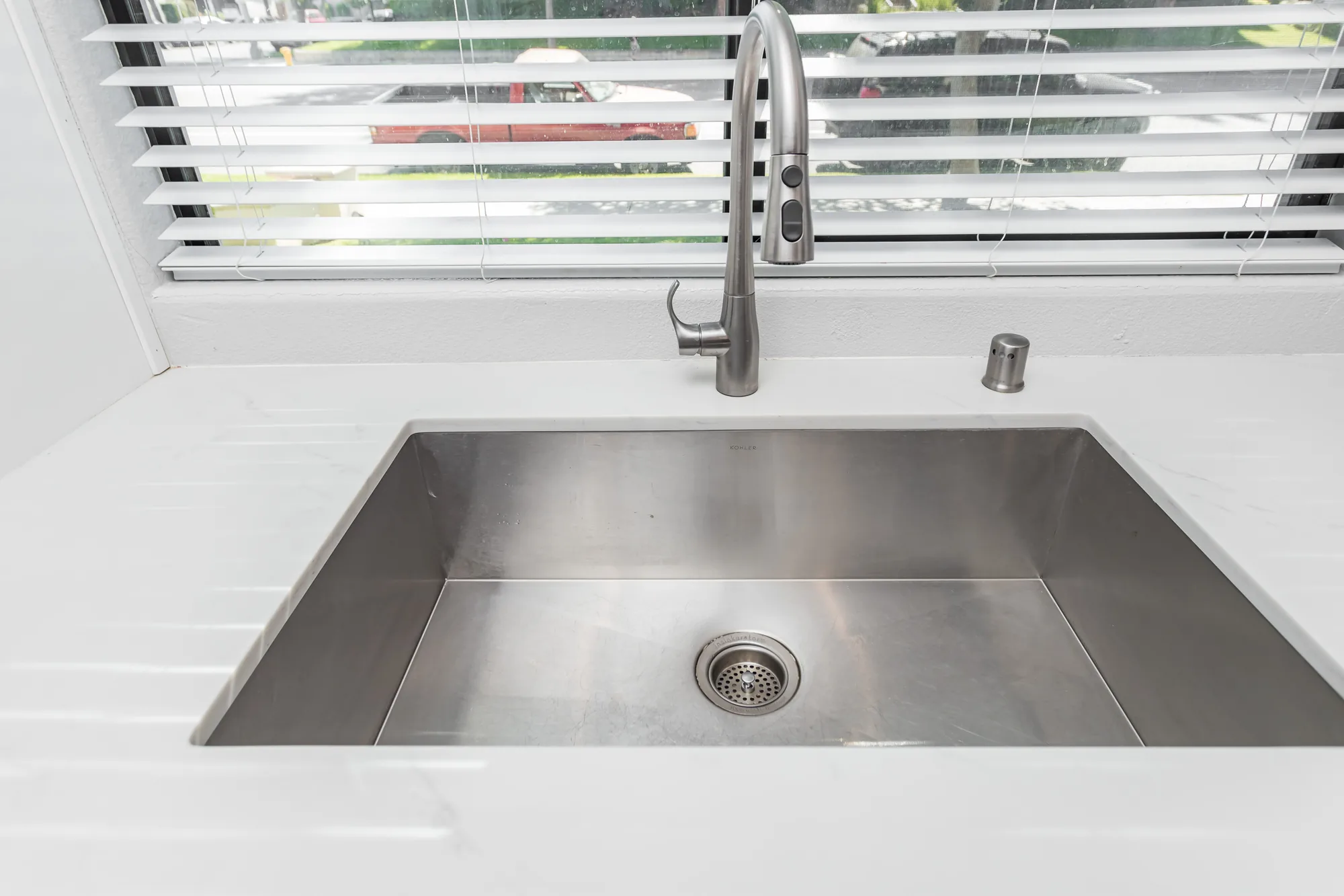 Close view of a deep undermount stainless sink set into a light countertop with a pull-down faucet.