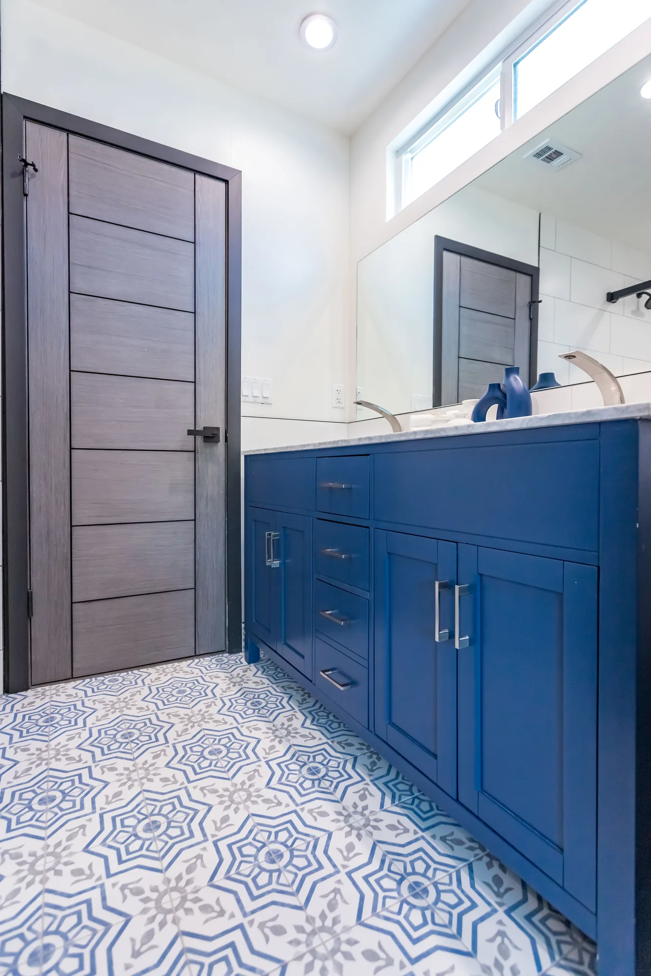 Navy vanity and gray woodgrain door above a blue patterned cement-look tile floor.