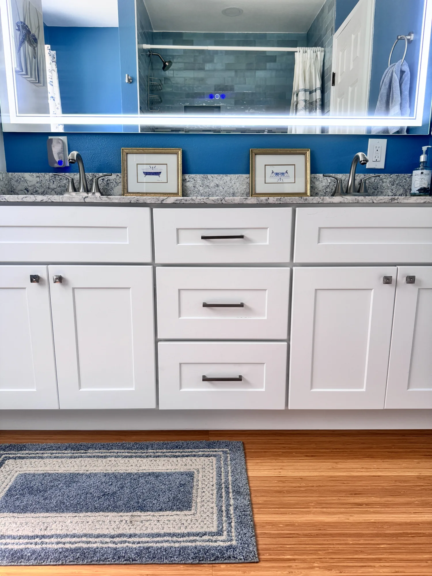 White shaker vanity cabinets and drawers below a stone-look counter, with wood-look flooring and a rug.