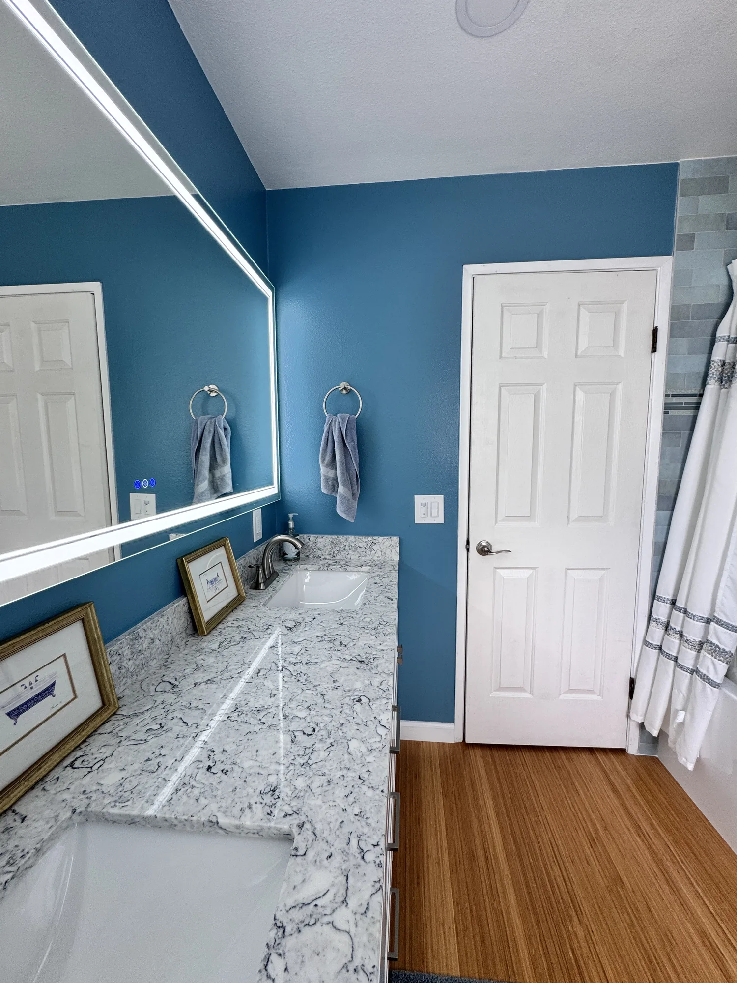 View along the vanity counter toward the white panel door, with towel rings on the blue wall.