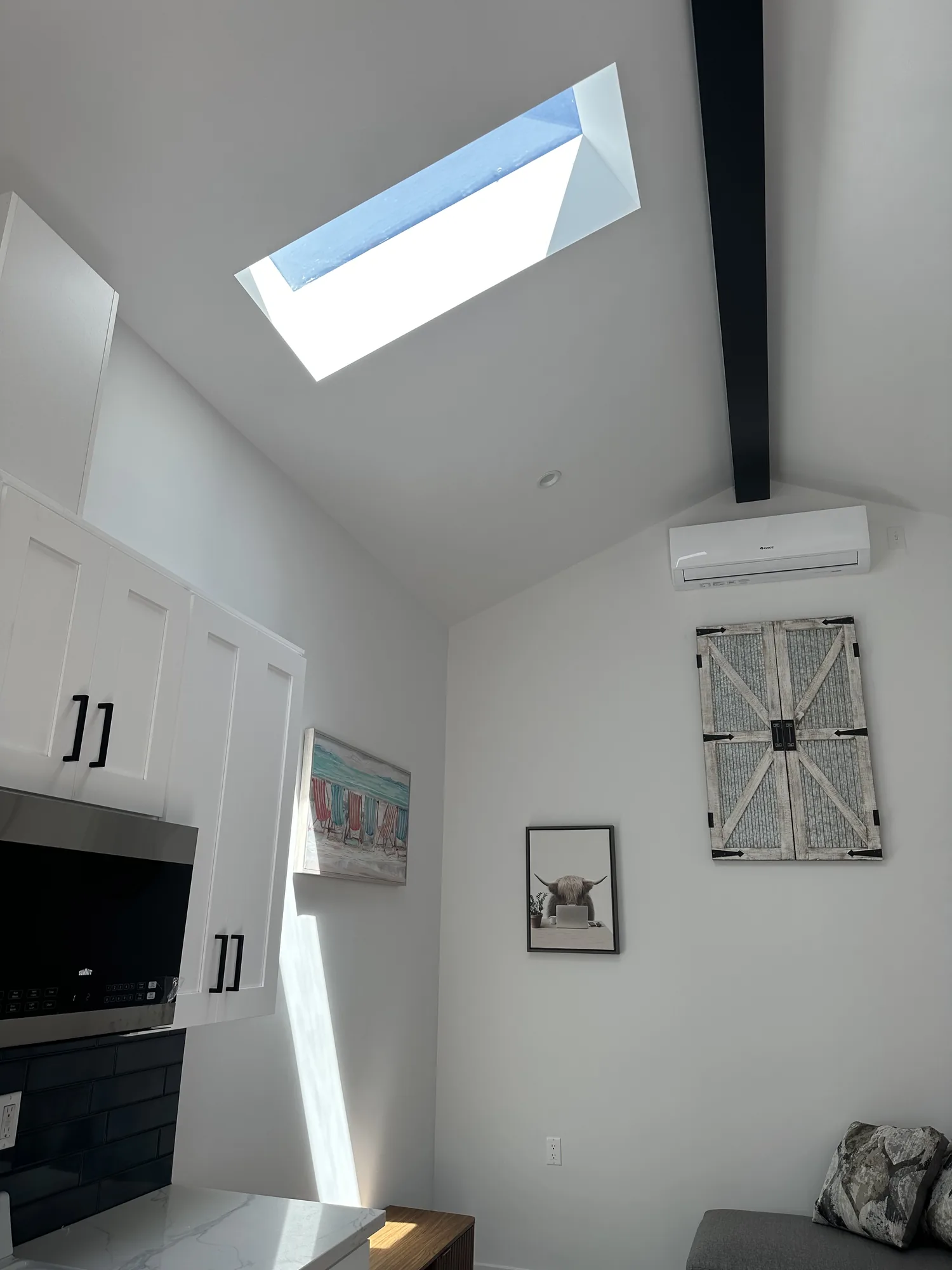 Vaulted ceiling detail with a long rectangular skylight and a dark exposed beam over the kitchenette.