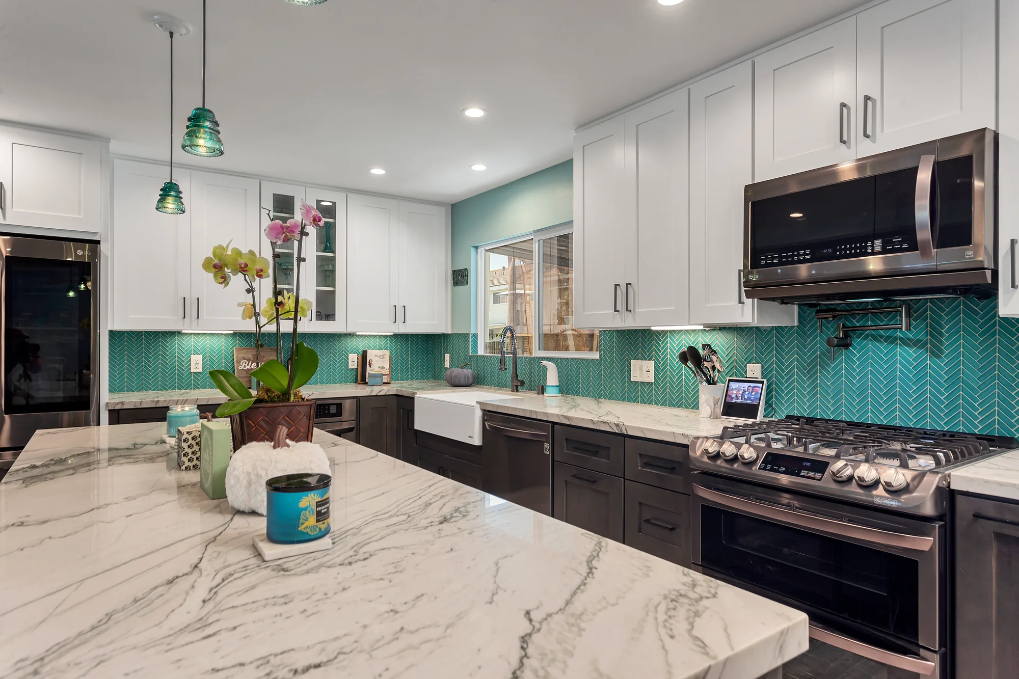 Veined white stone countertop leads toward a farmhouse sink and gas range under white shaker cabinets.
