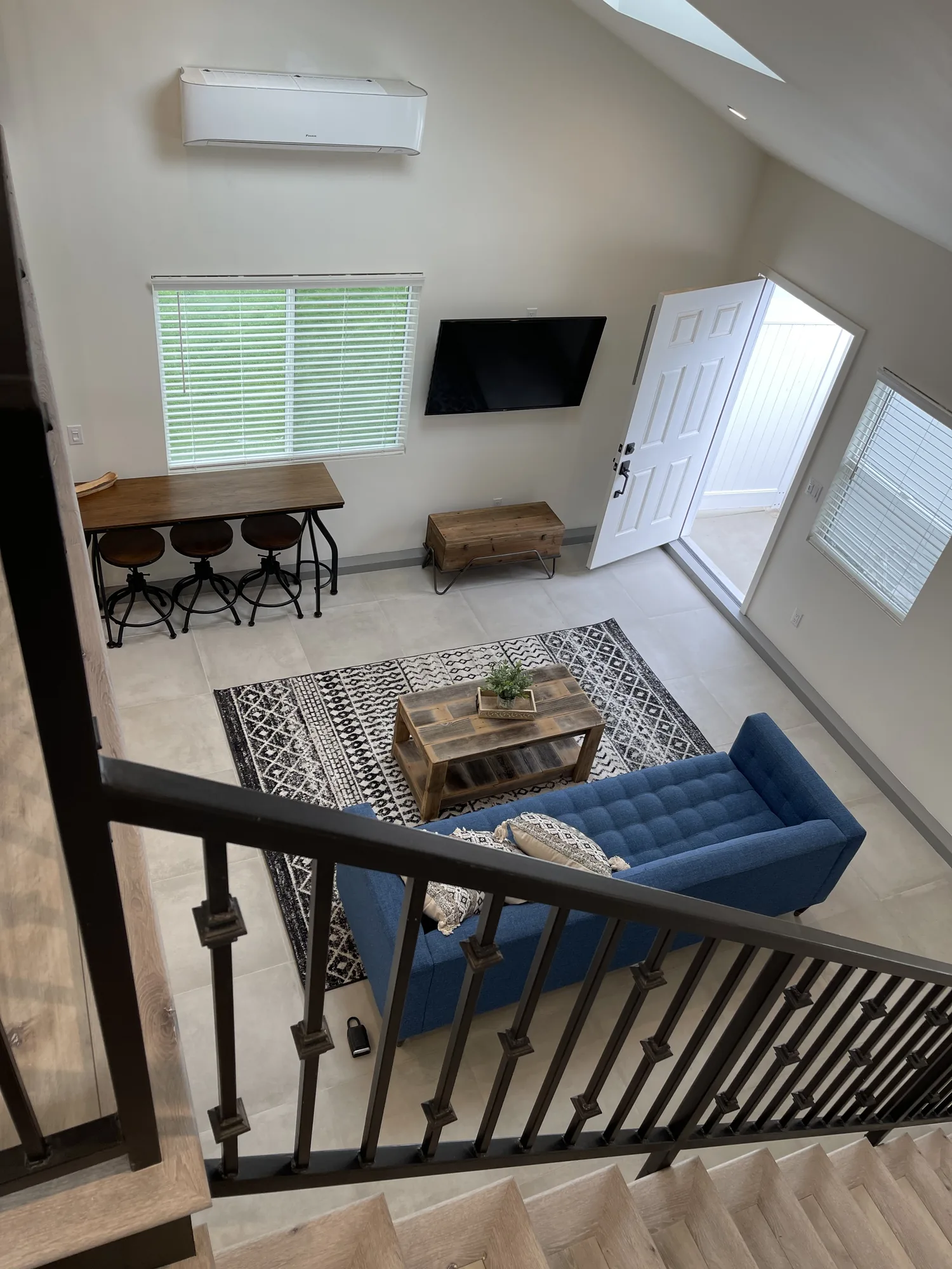Looking down from the loft railing to the living room with blue sofa, rug and counter stools.