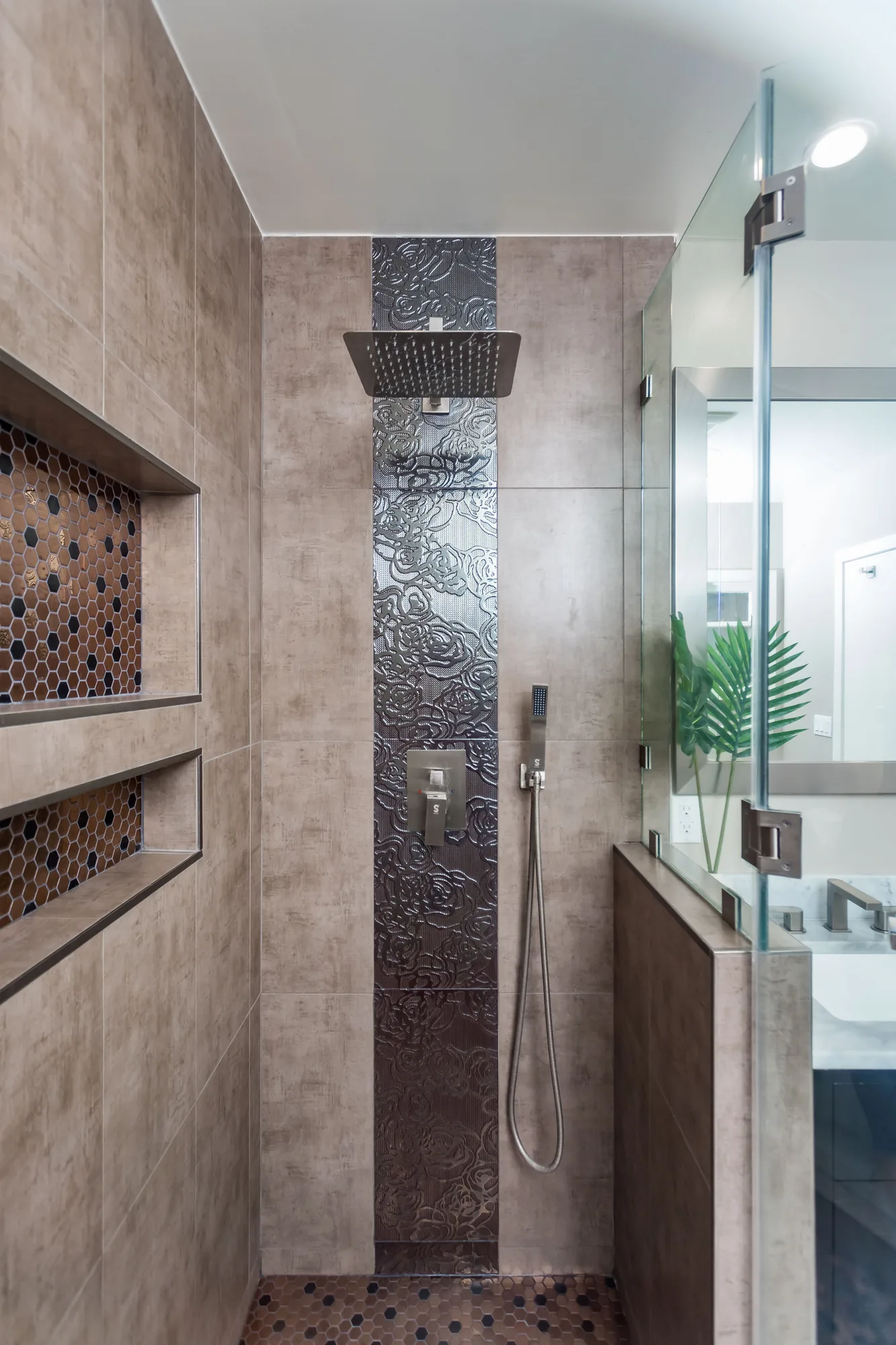 Narrow walk-in shower with a rain head, handheld sprayer and mosaic tile floor.