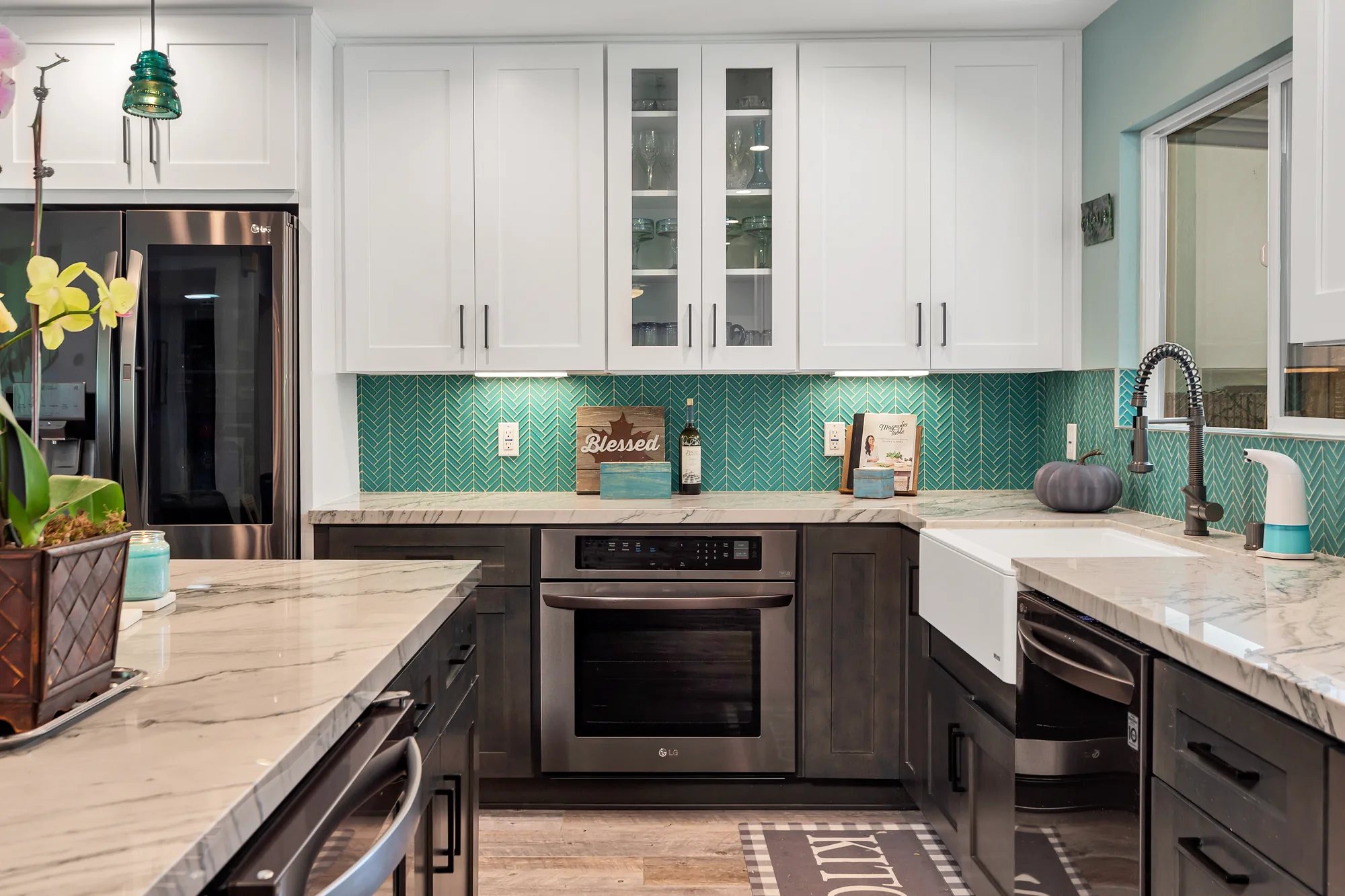 Built-in wall oven below glass-front cabinets beside a farmhouse sink and teal herringbone backsplash.
