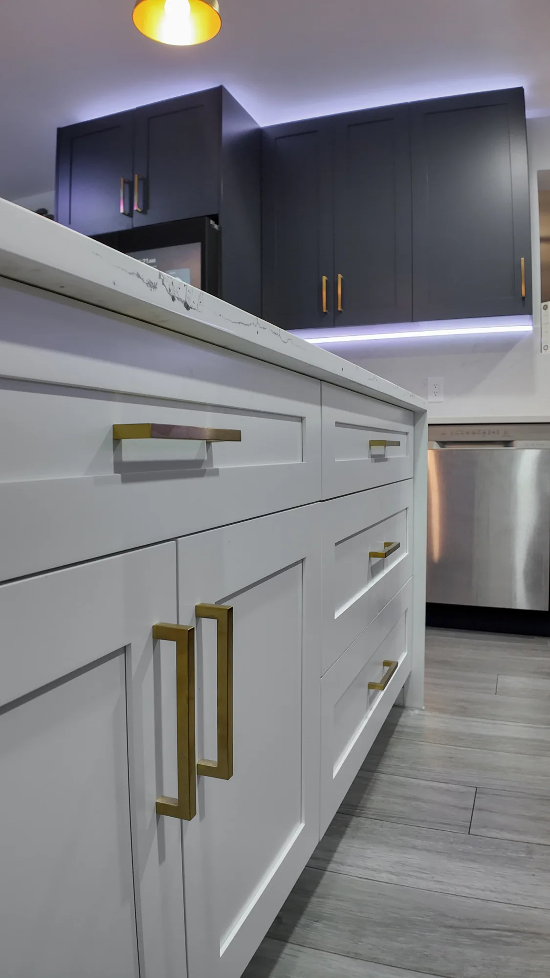 Close view of white shaker island drawers and doors fitted with long brushed brass bar pulls.
