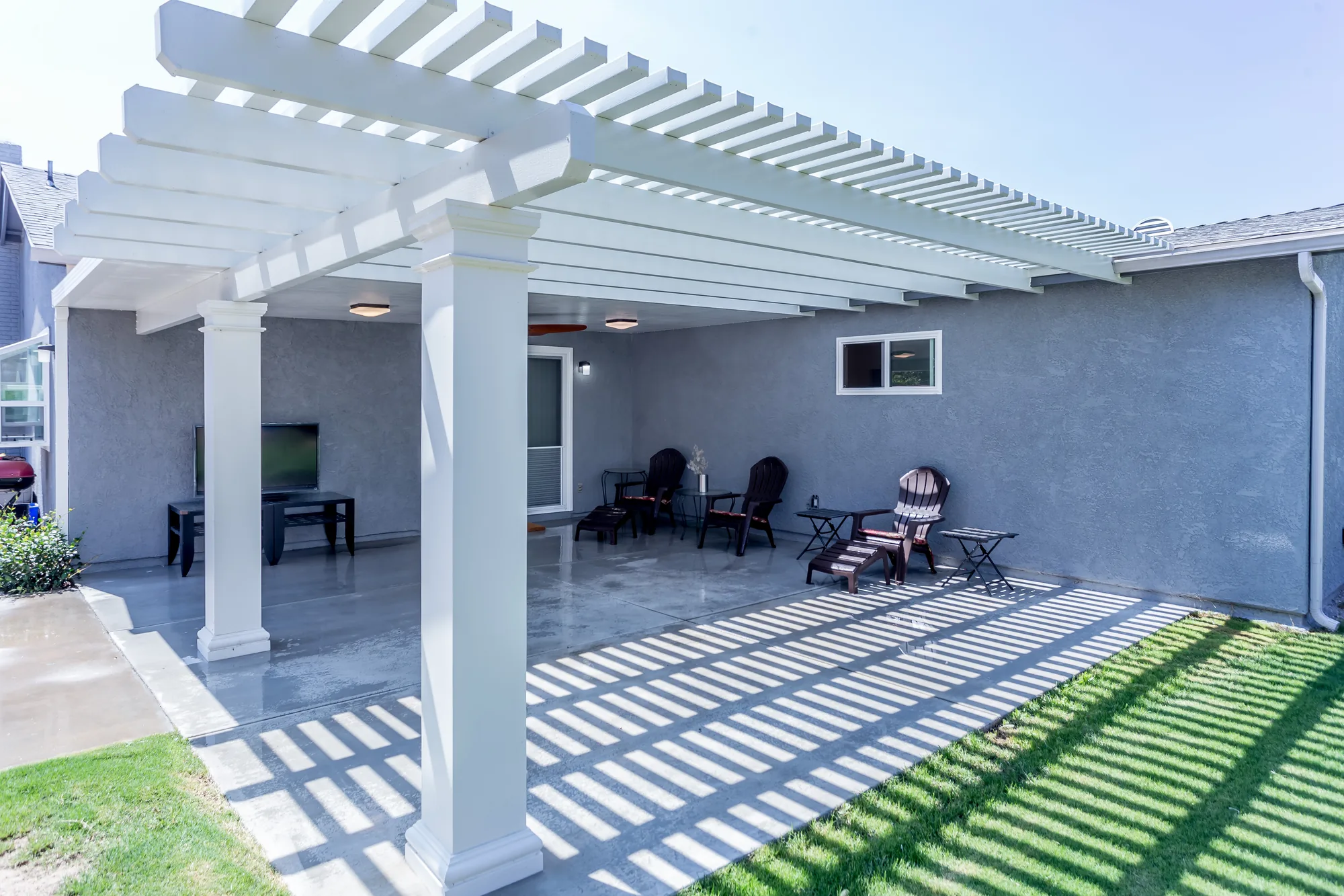 White pergola patio cover with square columns attached to a gray stucco home over a concrete patio.
