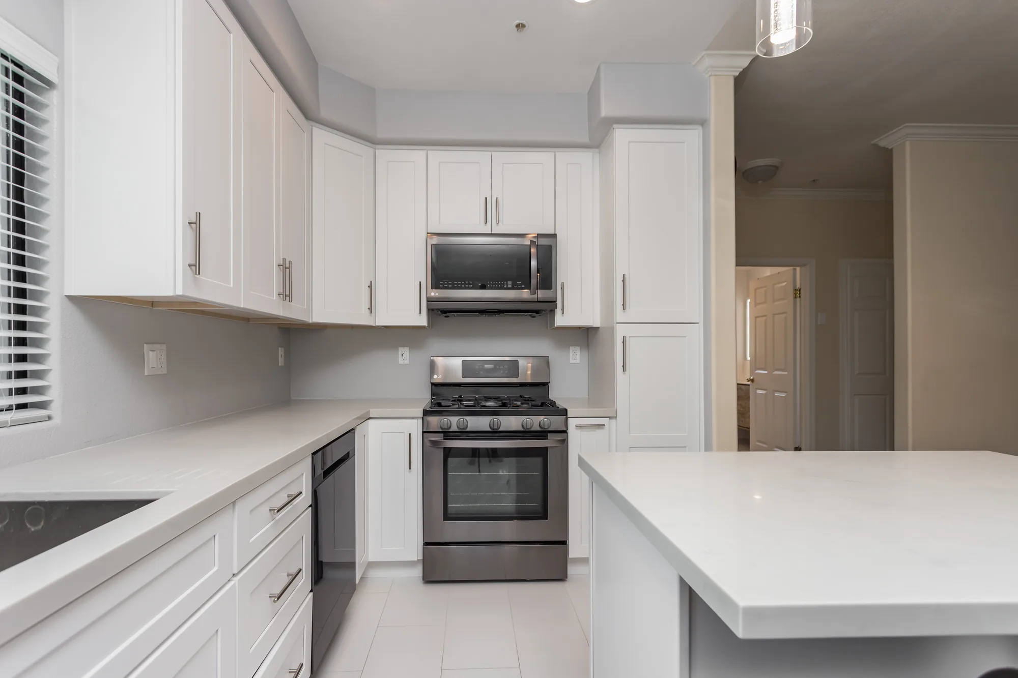 Finished white shaker kitchen with a stainless gas range, microwave, and light quartz-look island counter.