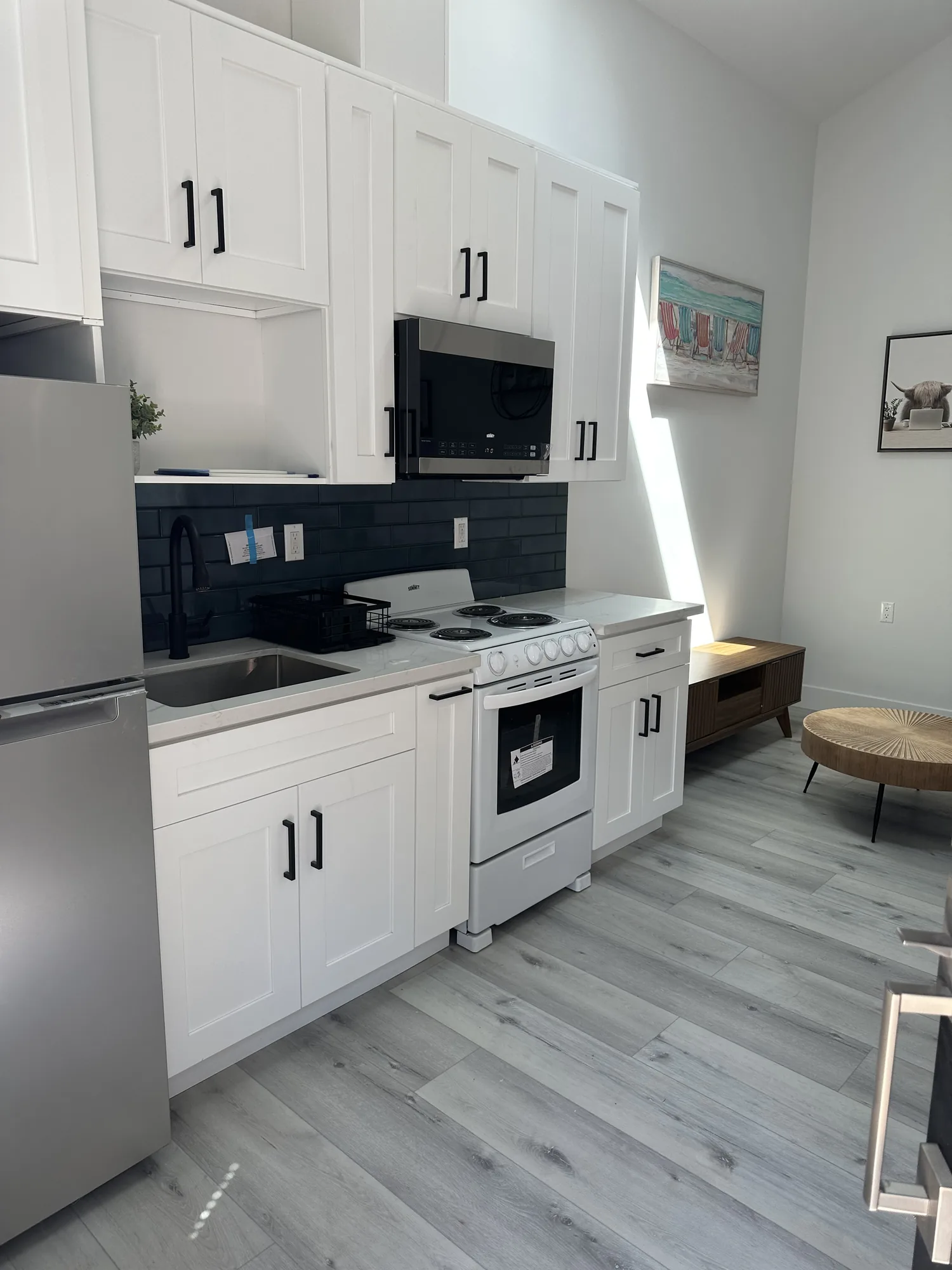 Kitchenette with white shaker cabinets, dark subway tile backsplash and stainless appliances.