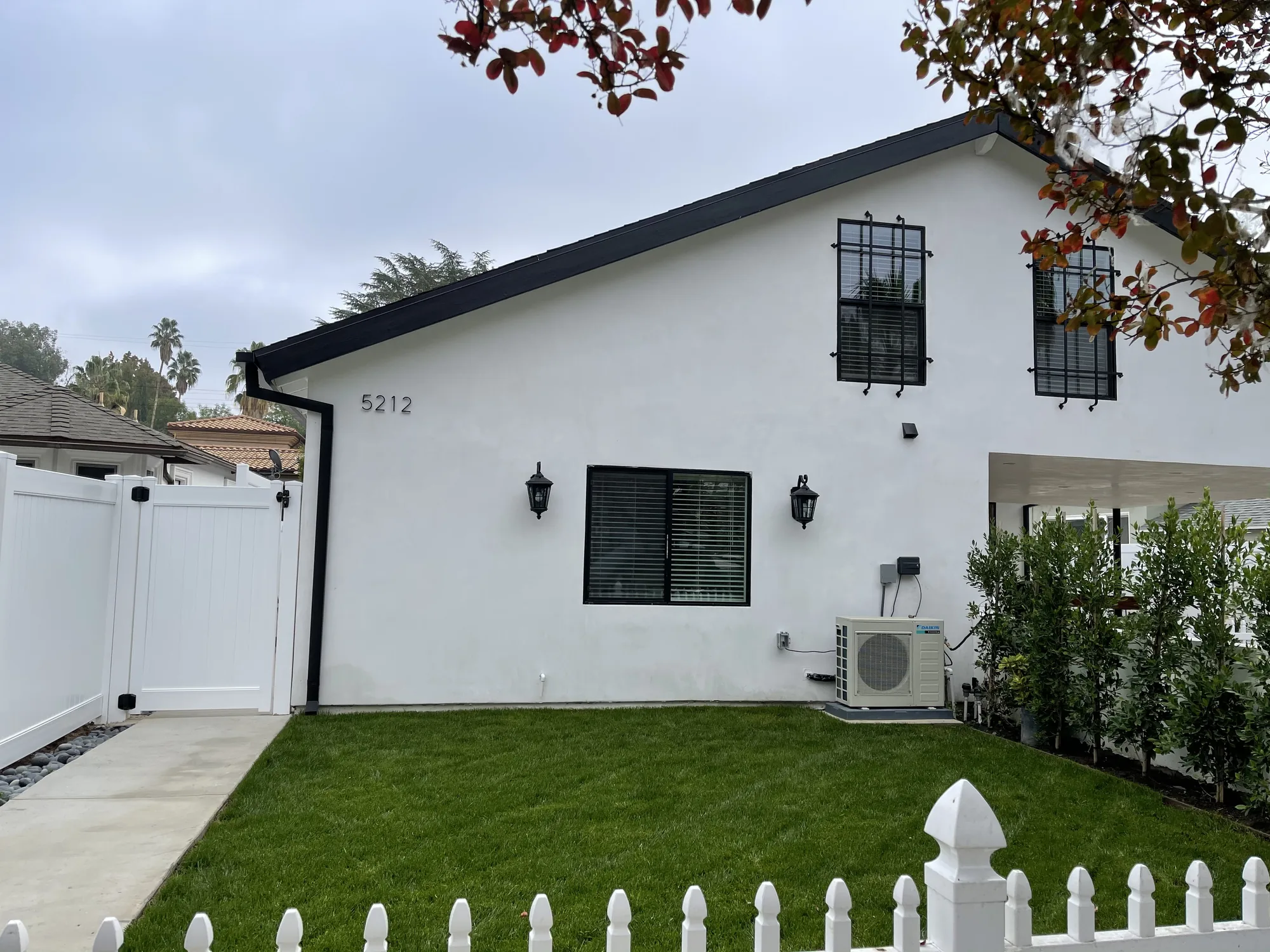 Exterior elevation of a white stucco dwelling with dark fascia, black window grilles and a lawn.
