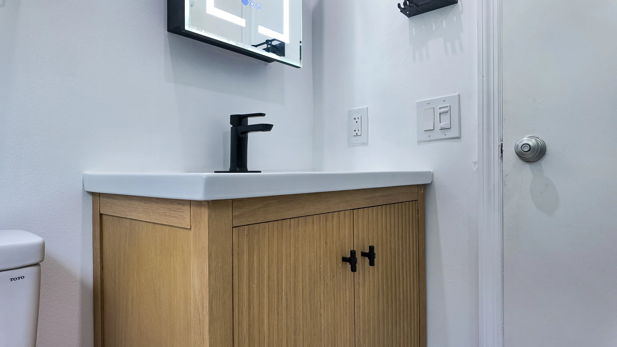Angled view of a fluted wood vanity with matte black knobs, black faucet and white integrated sink top.